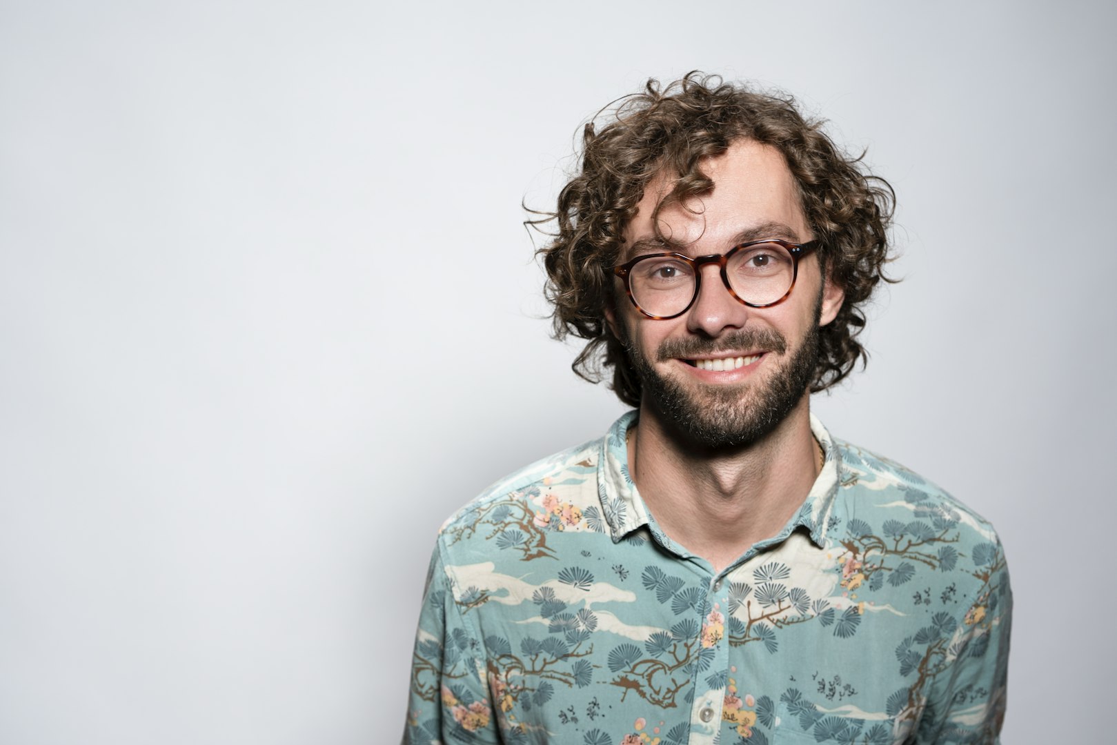 A man in a light blue polo shirt standing in front of a shelf filled with various kitchen items and textiles. The background is softly blurred, drawing focus to his friendly expression and casual style.